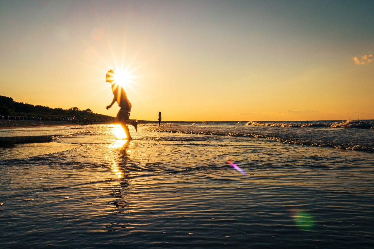 Silhouette einer Person beim Laufen am Strand gegen die untergehende Sonne.