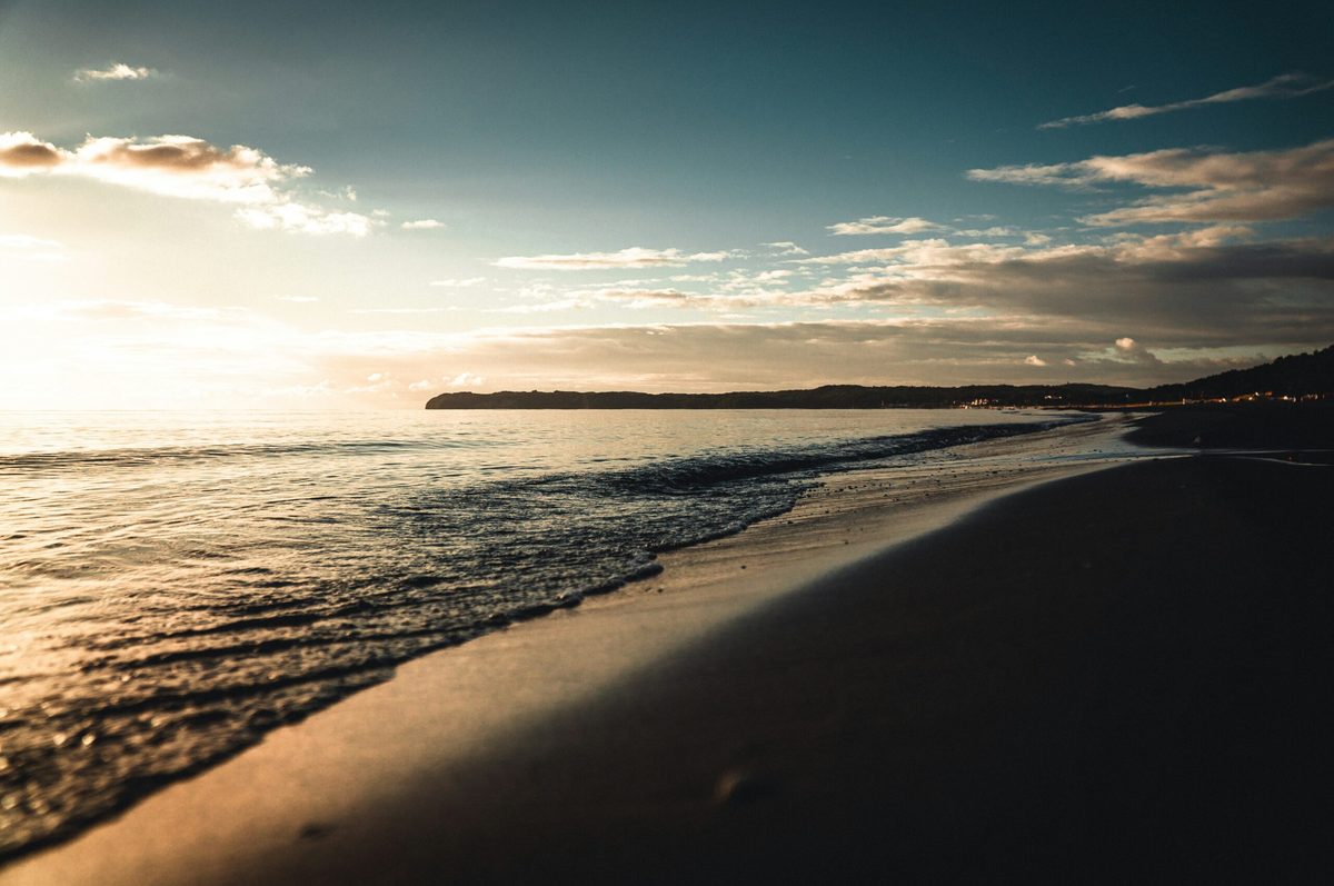 Strandpanorama bei Sonnenuntergang mit weichem Licht und langen Schatten.