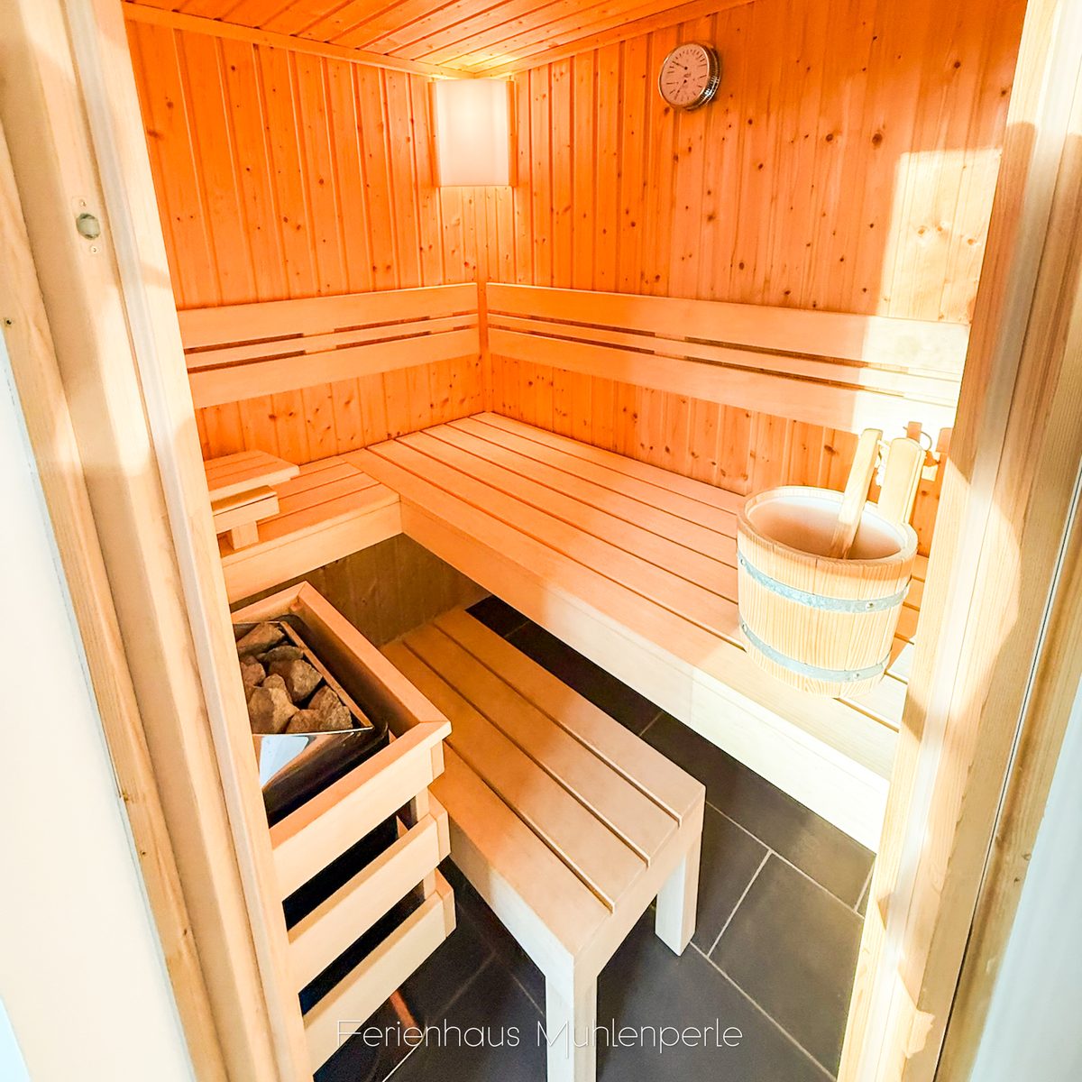 Private Sauna im Ferienhaus Mühlenperle mit Holzbänken, Aufgusseimer und Saunaofen.
